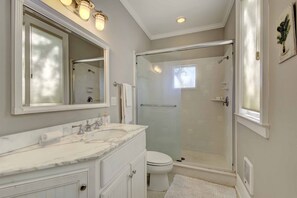 A bathroom with a marble vanity, a large mirror, a toilet, and a glass-enclosed shower.