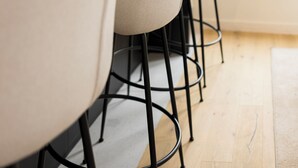 A row of modern chairs with black metal legs and a light-colored cushion, positioned in front of a window with a view of buildings.