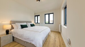 A modern bedroom with a large bed, bedside tables, and a view of the city through windows.