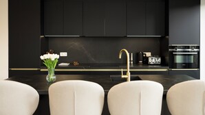 A modern kitchen with black cabinets, a marble countertop, a gold faucet, and a vase of white flowers.