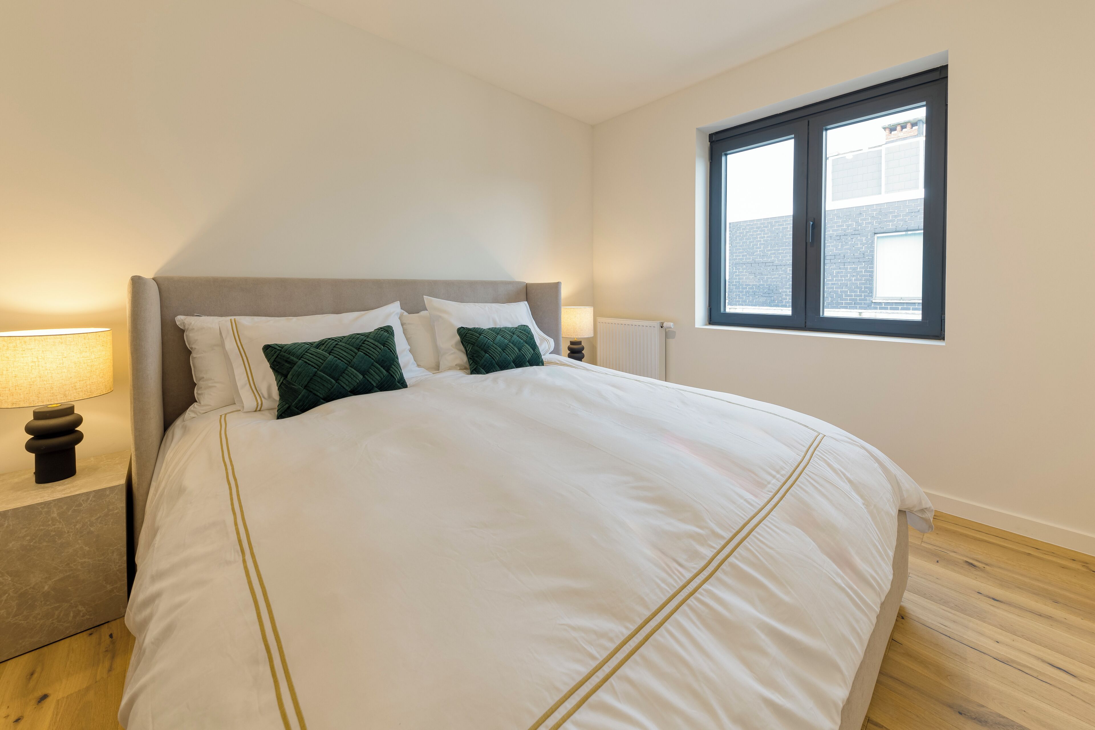 Une chambre avec un grand lit, deux tables de chevet, une fenêtre et un radiateur.