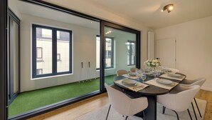A dining area with a table set for four, large windows, and a view of a green space outside.