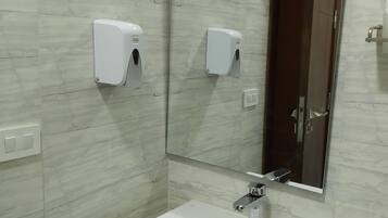 Une salle de bain avec un lavabo blanc, deux distributeurs de savon, un miroir et une porte.