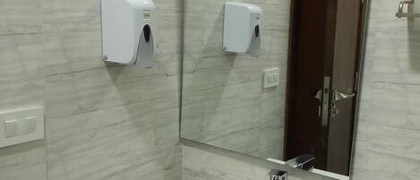 A bathroom with a white sink, two soap dispensers, a mirror, and a door.