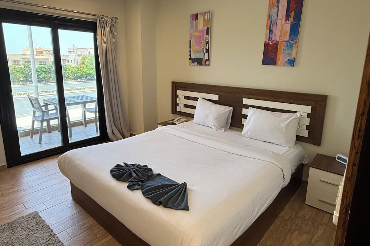A hotel room with a large bed, a bedside table, a nightstand, a window with curtains, and artwork on the wall.
