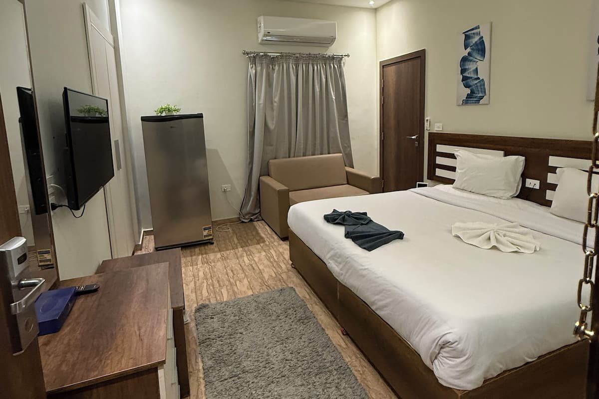 A modern hotel room with a bed, a desk, a TV, an air conditioning unit, and a grey rug.
