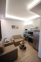 A compact living space with a sofa, a small coffee table with fruit, a microwave, a stove, and a washing machine.