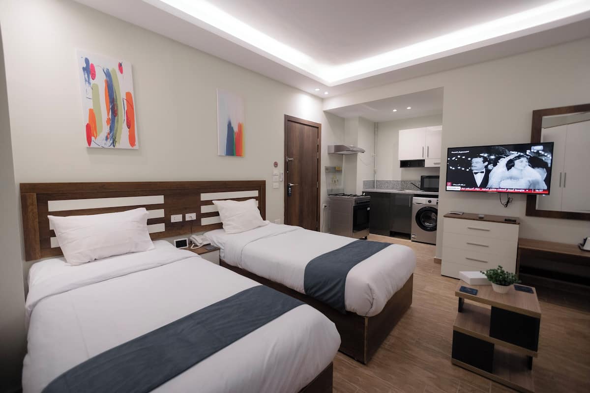 A hotel room with two beds, a TV, a small kitchen area, and a washing machine.