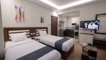 A hotel room with two beds, a TV, a small kitchen area, and a washing machine.