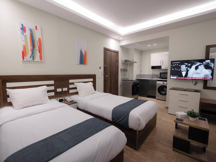 A hotel room with two beds, a TV, a small kitchen area, and a washing machine.