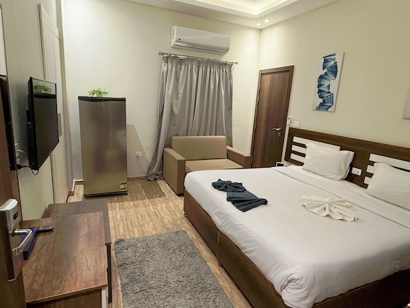 Habitación de hotel con cama, escritorio, silla, equipo de aire acondicionado, televisor y puerta.