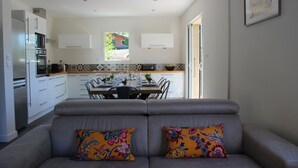 Et moderne køkken med hvide skabe, et spiseområde med et bord og stole, og en grå sofa med farverige puder.