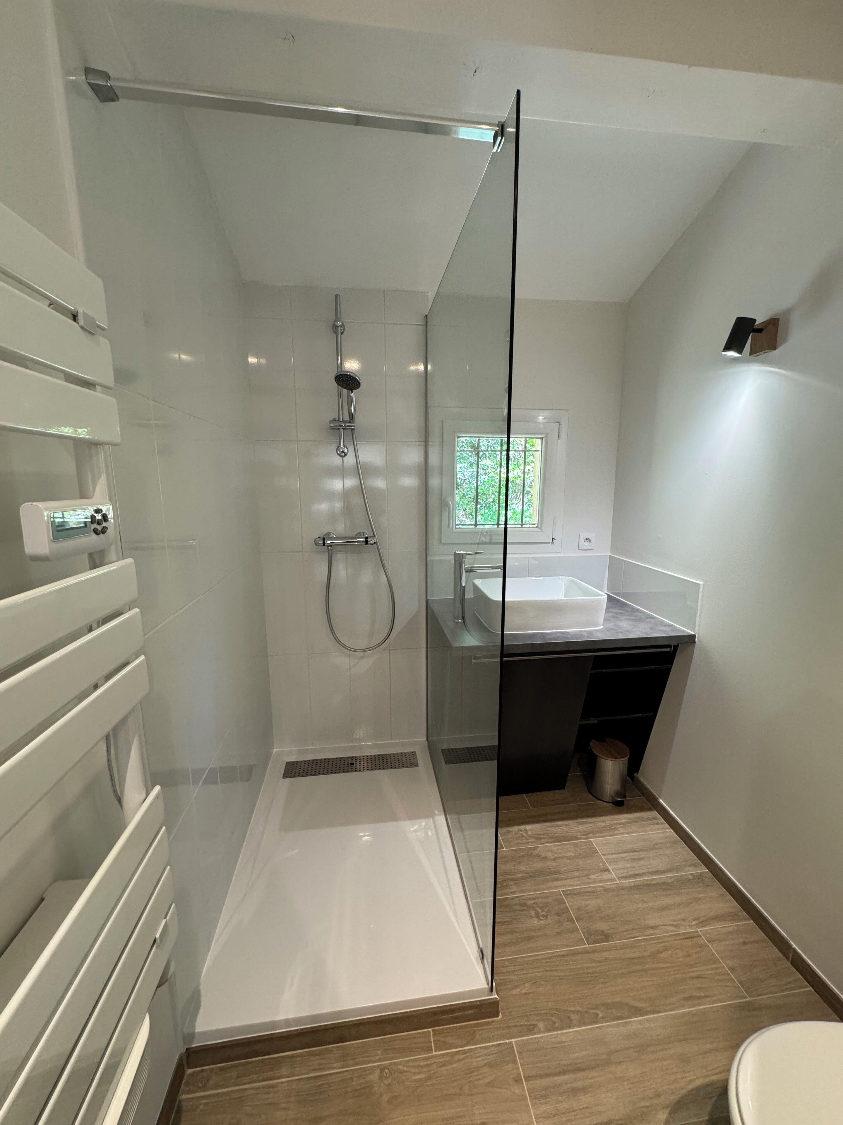 A modern bathroom with a glass-enclosed shower, a white sink, and a wooden floor.
