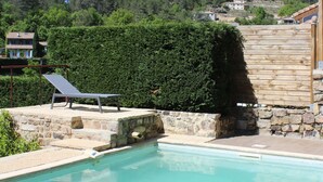 En swimmingpool med stenterasse, et træhegn og udsigt til en bakke med huse.