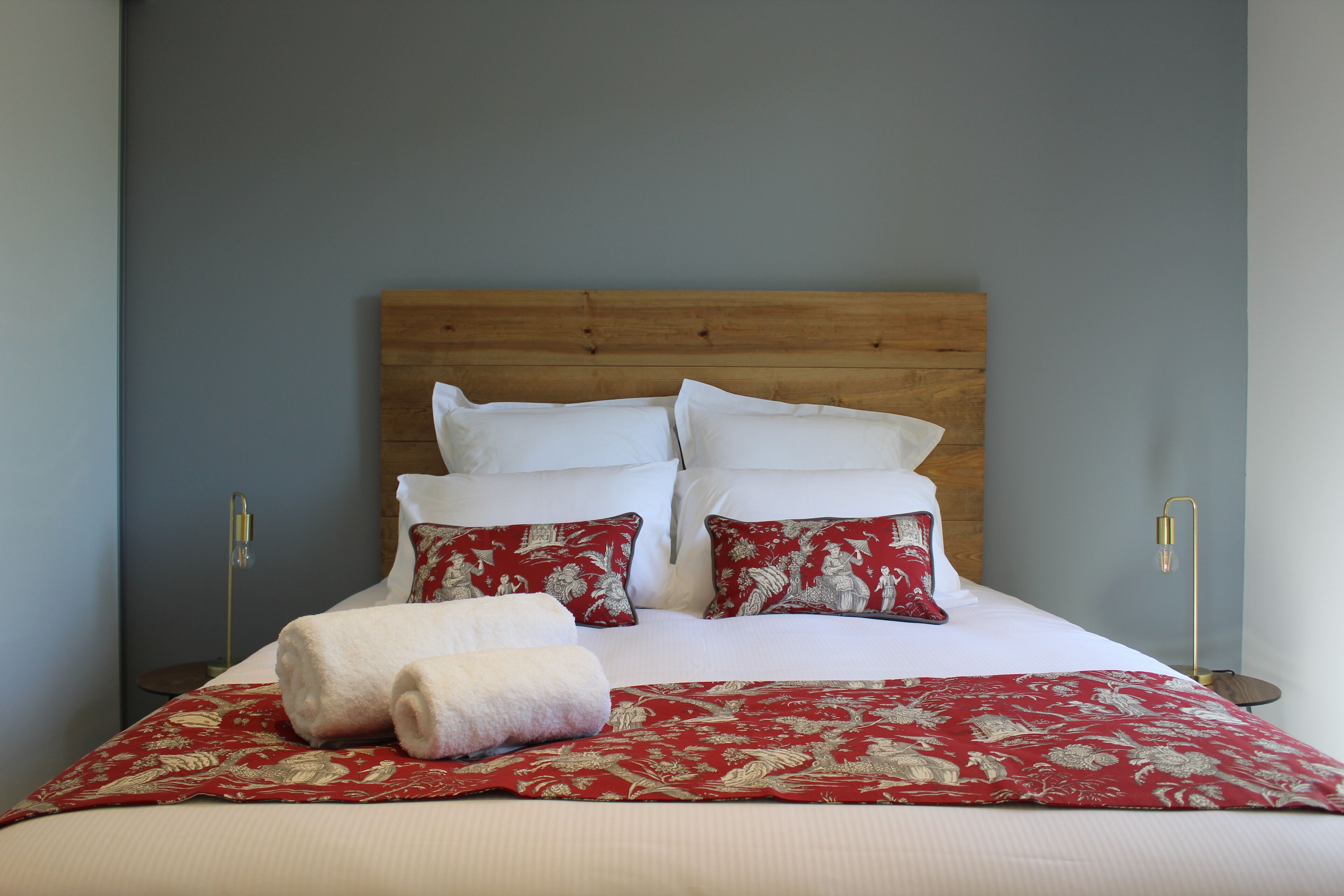 Un lit bien fait, avec une literie blanche et rouge, une tête de lit en bois et deux tables de chevet avec des lampes.