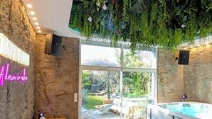 Un área interior moderna para relajarse, con pared de piedra, letrero de neón, jacuzzi y vistas al exterior.