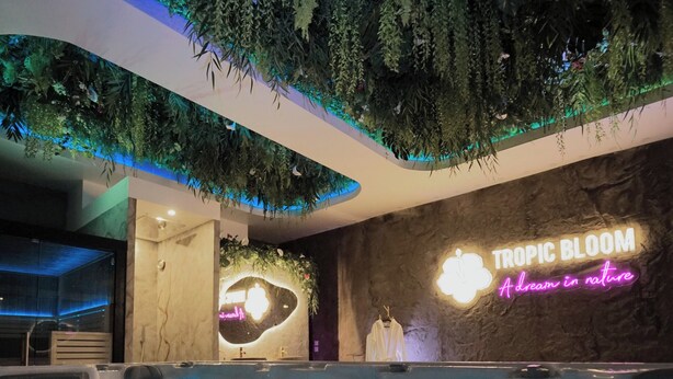 Un área de piscina interior moderna con un letrero de neón que dice "TROPIC BLOOM A dream in nature".