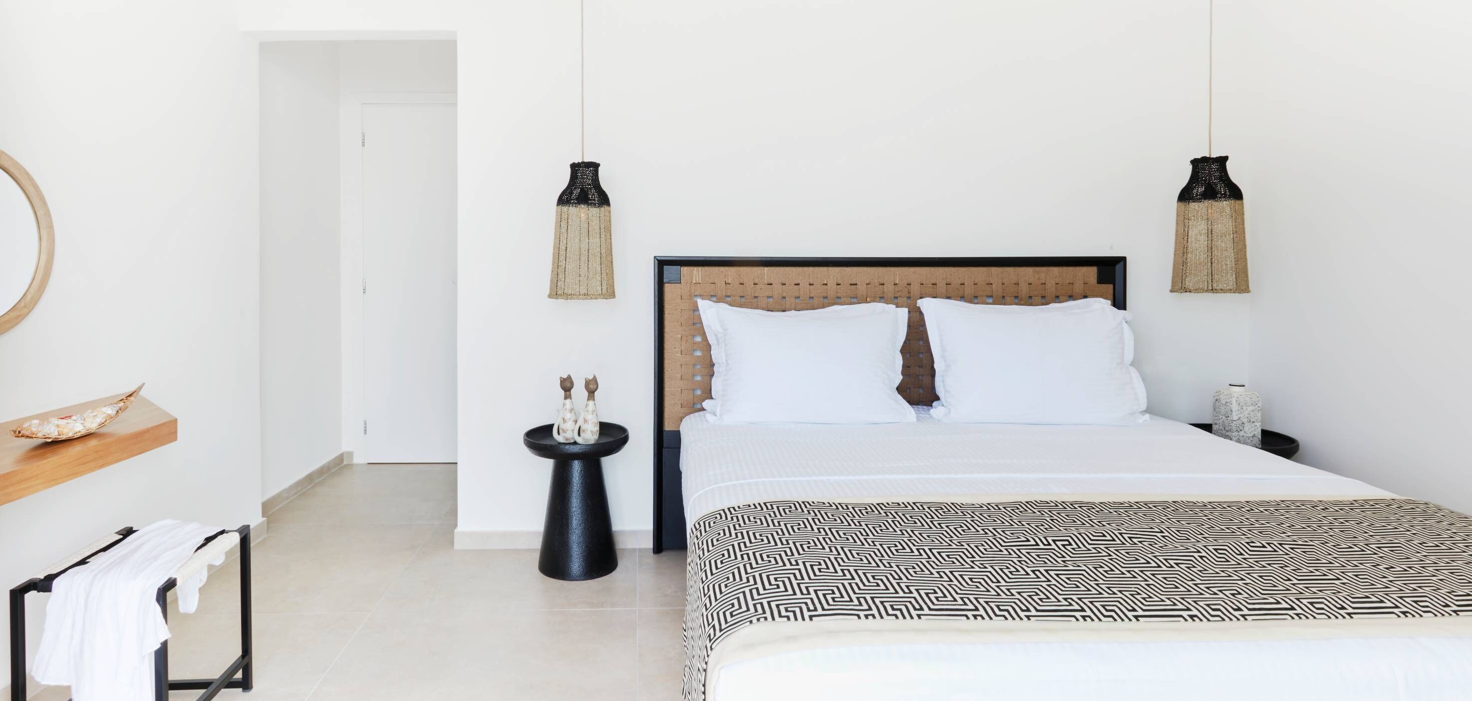 Un dormitorio moderno con una cama, un espejo redondo, una mesita con adornos y dos lámparas colgantes.