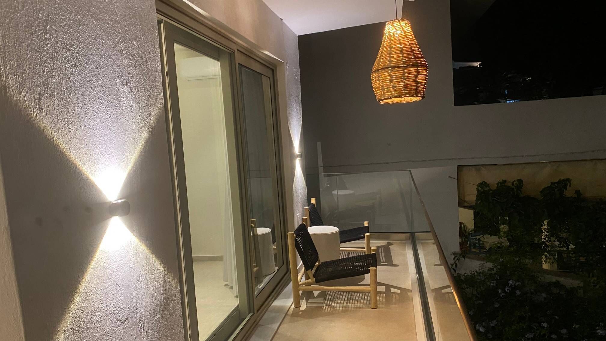 Een balkon met buiten, voorzien van een glazen deur, een hanglamp van riet, een stoel en een kleine tafel.