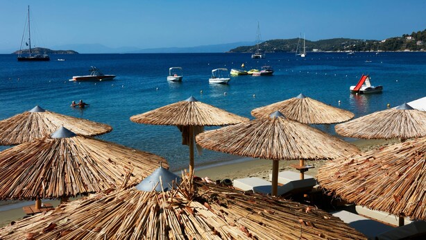 A beach with thatched umbrellas and boats on the water. - Skiathos Ammos Luxury Apartments in Megali Ammos Beach (Skiathos)