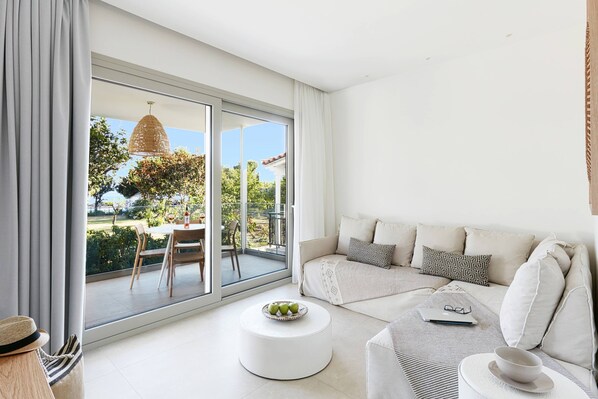 A modern living room with a sofa, a round coffee table, and a dining area visible through a sliding glass door.