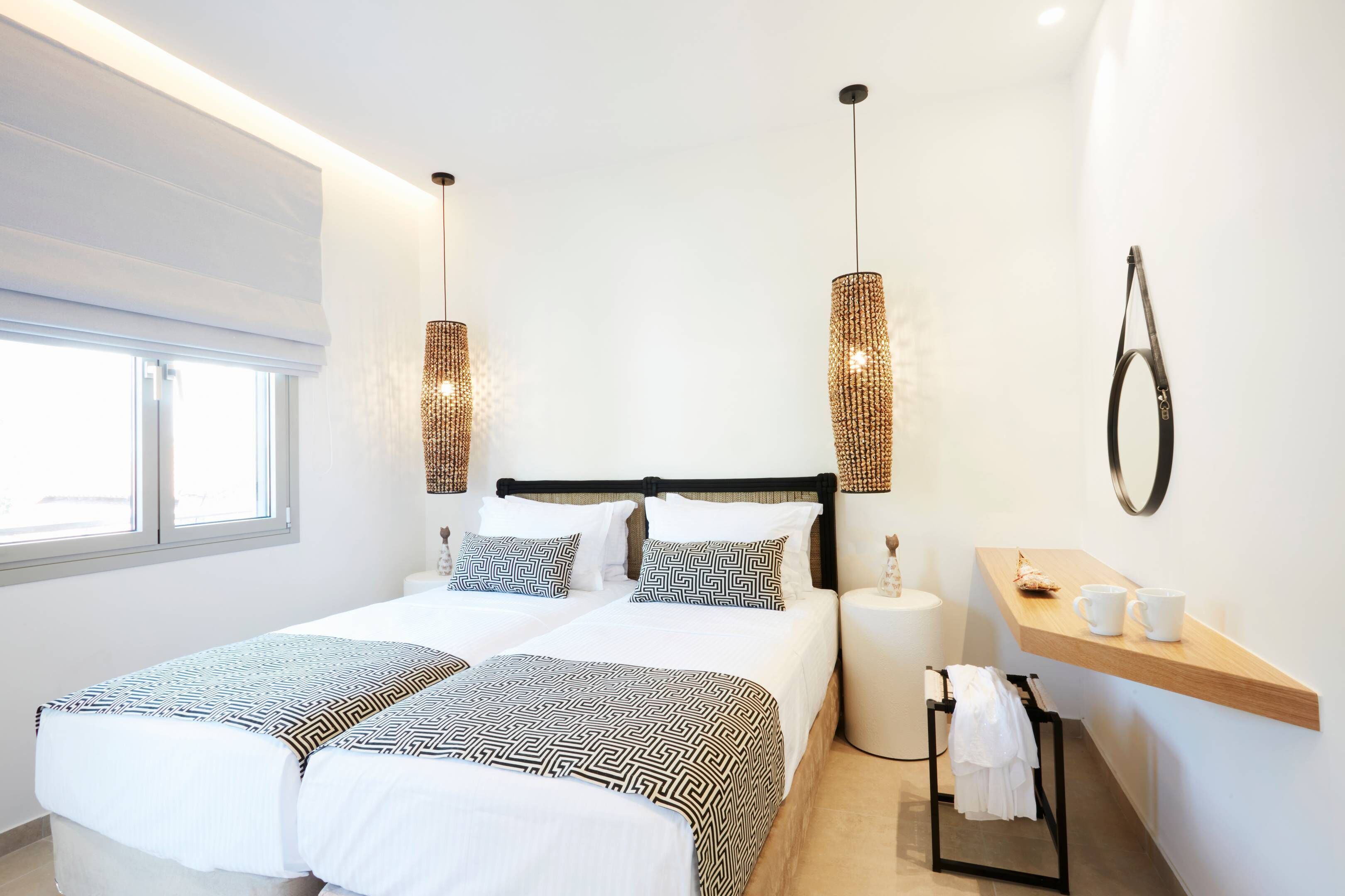 A modern hotel room with a large bed, two bedside tables, a small wooden shelf, and a window.