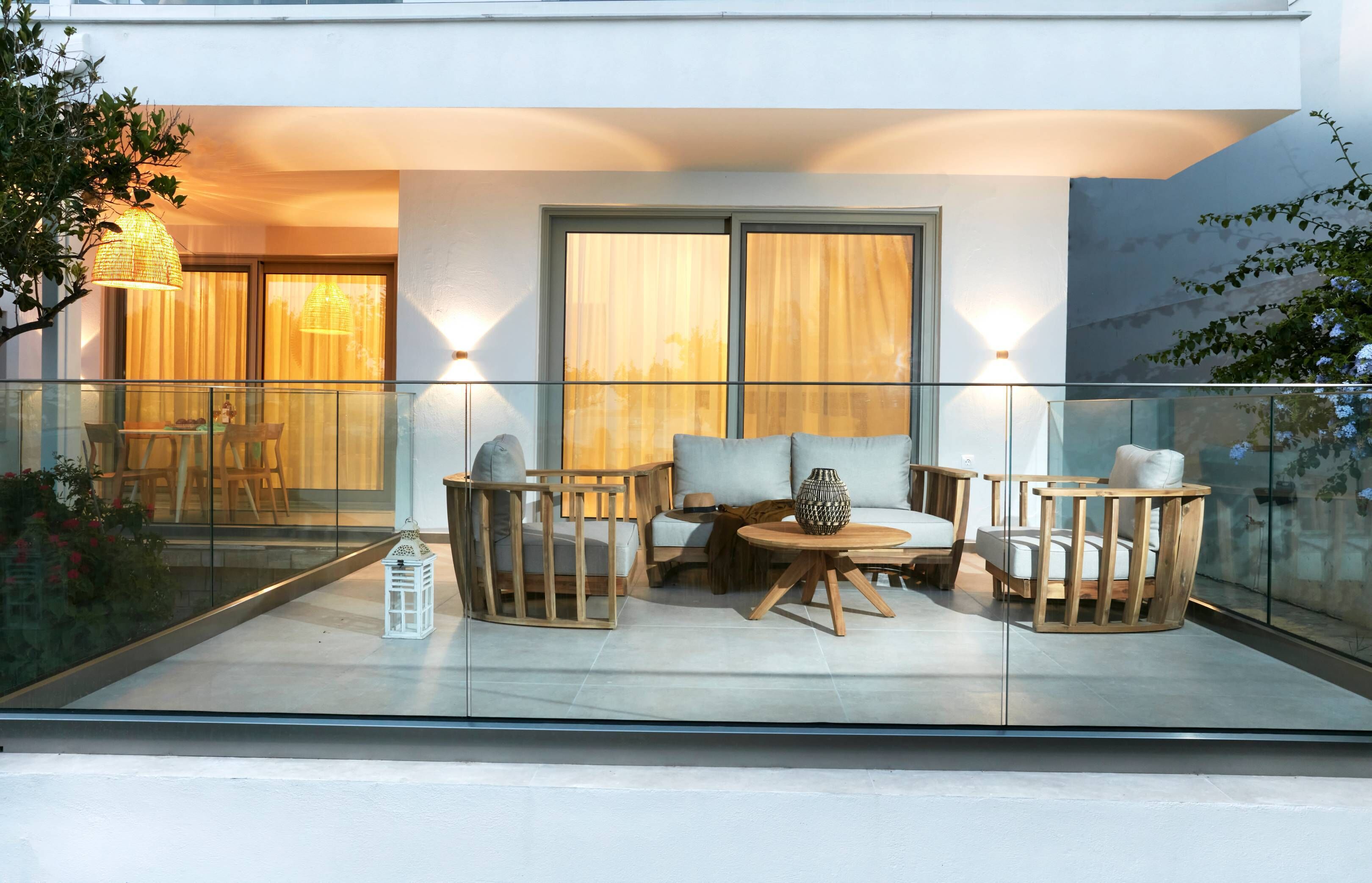 A modern outdoor seating area with a glass balustrade, cushioned chairs, a round table, and a lantern.