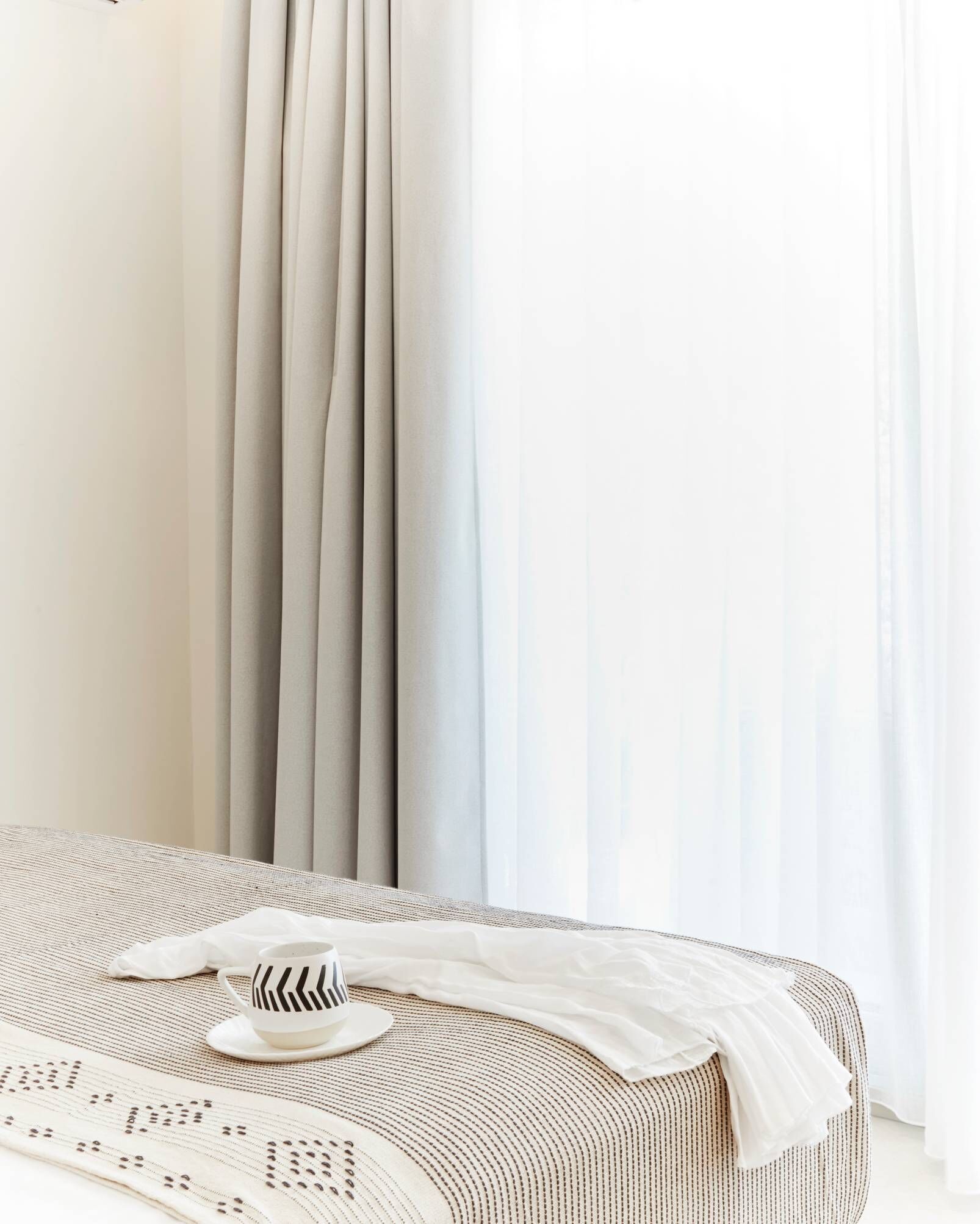 A bed with a striped bedspread, a white pillow, and a white cup with a black pattern.