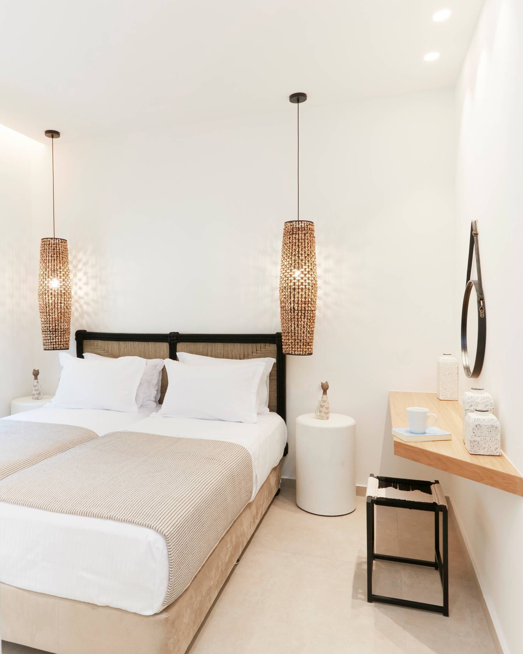 A modern bedroom with a bed, two hanging lamps, a bedside table with a cup, and a small stool.