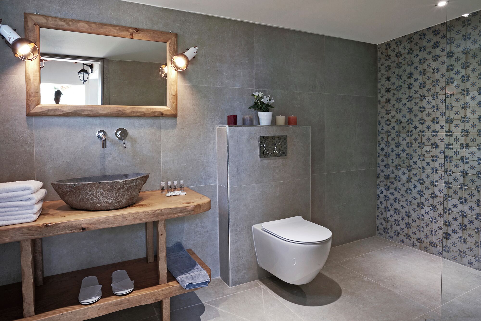 Un baño con tocador de madera, un lavabo grande, un espejo con iluminación y un inodoro, además de baldosas estampadas.