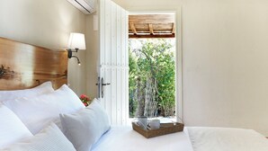 A bedroom with a bed, a nightstand, a lamp, a window, and a view of trees. - Villa Ira Skiathos Luxury Villa (Skiathos)