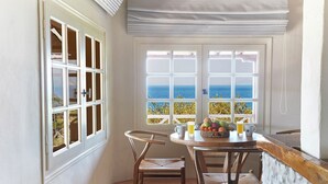 A small dining area with a table, chairs, and a view of the sea through large windows. - Villa Ira Skiathos Luxury Villa (Skiathos)
