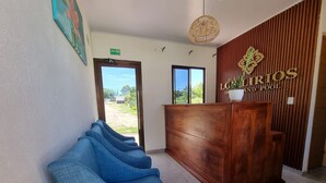A reception area with a wooden desk, a sign reading "LURIOS HOTEL AND POOL", and a blue bench. - Los Lirios Hotel  (El Coco)