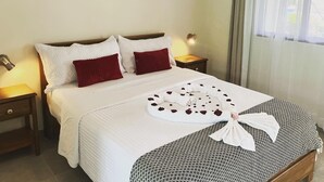 A neatly made bed with white and red pillows, a decorative bow, and a heart-shaped arrangement of rose petals on the bedspread. - Los Lirios Hotel  (El Coco)