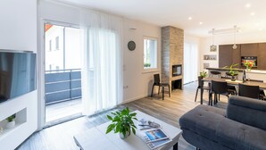 Un salon moderne doté d’un téléviseur à écran plat, d’un canapé gris, d’un coin repas avec une cuisine en arrière-plan et d’un balcon avec une porte coulissante.