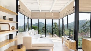 Un salon moderne avec un canapé, une table basse et un téléviseur. De grandes fenêtres offrent une vue sur l’extérieur.