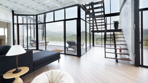 Un intérieur moderne avec un espace de vie délimité par des parois de verre, un escalier et une vue sur l’extérieur.