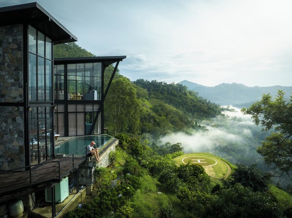 A modern building with a glass exterior, a pool, and a view of a lush valley with mountains in the background. - Walaa Kulu – A Villa by 98 Acres (Ella)