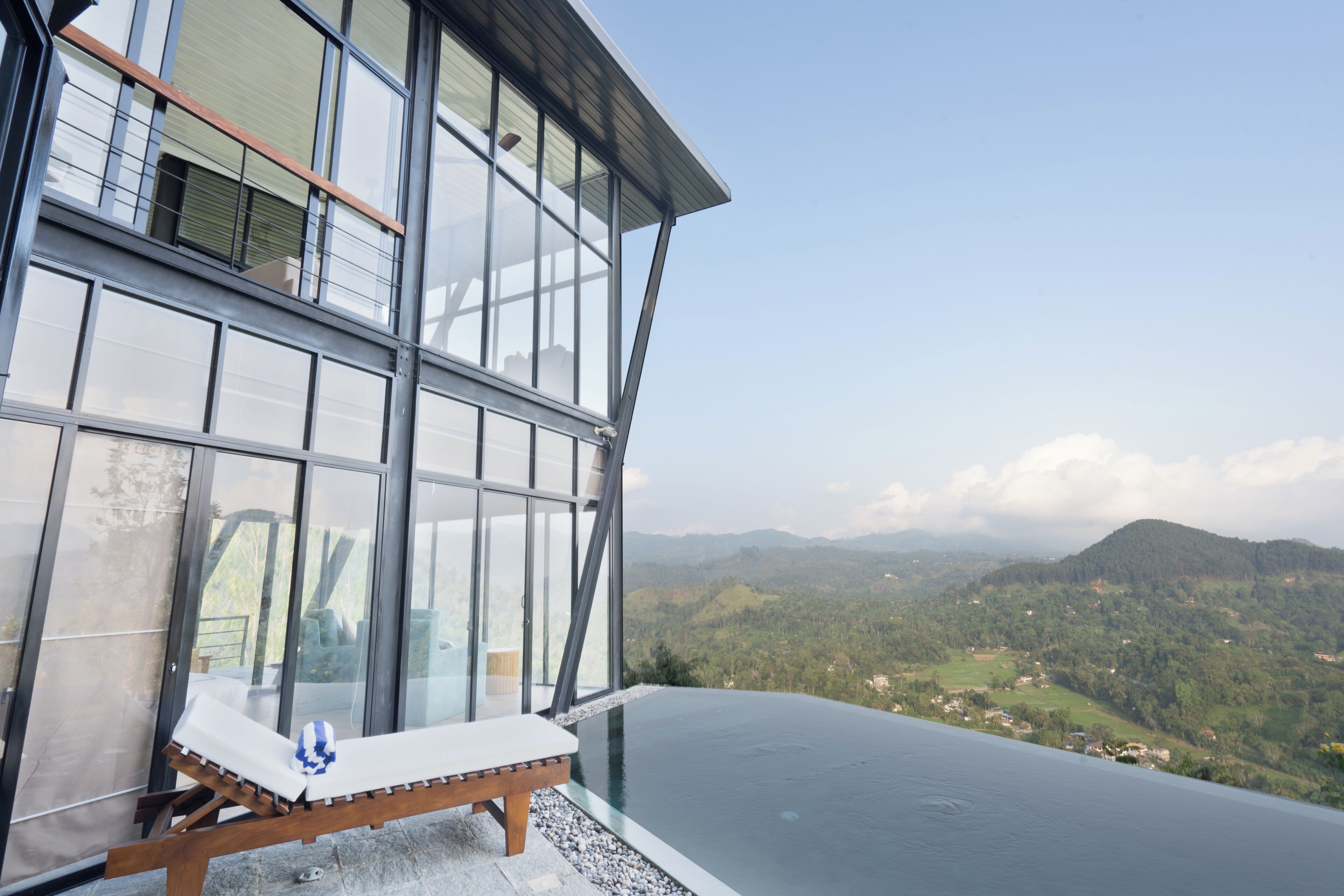 A modern building with large glass windows, a wooden lounge chair, and a view of a mountainous landscape.