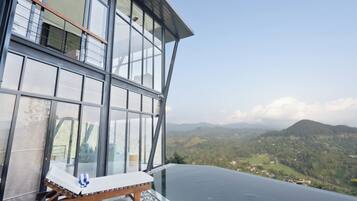 A modern building with large glass windows, a wooden lounge chair, and a view of a mountainous landscape.