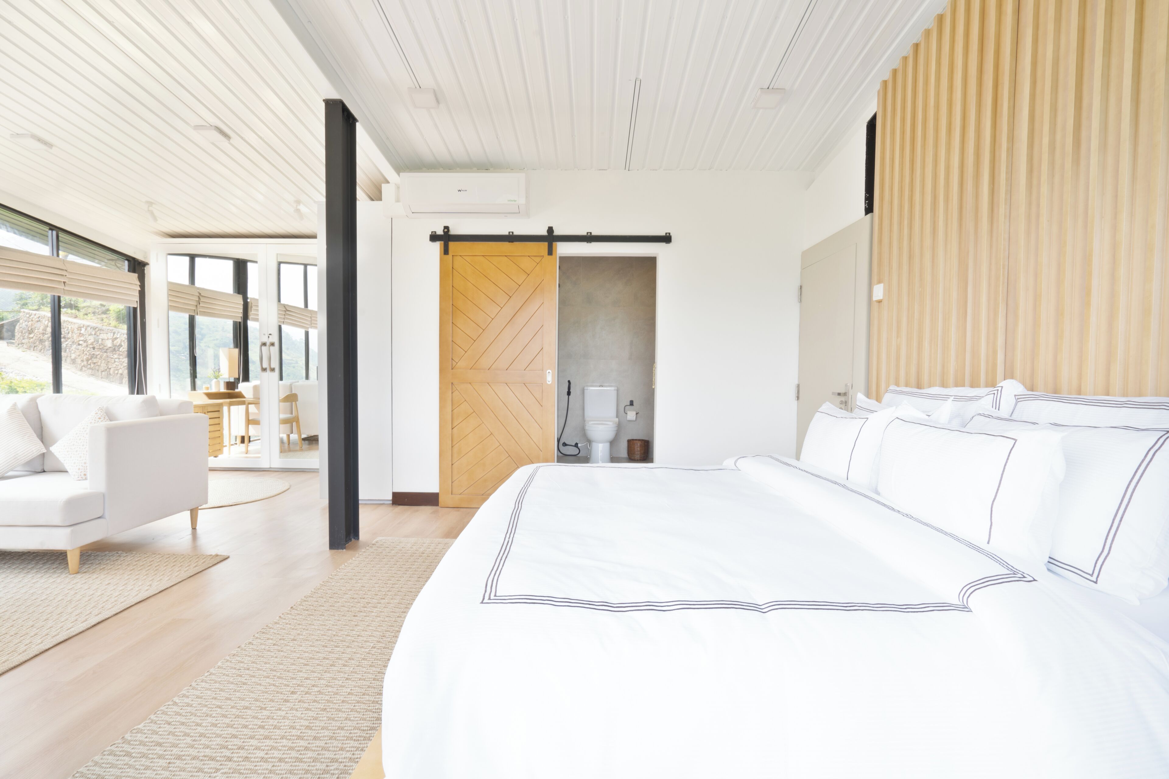 Een moderne slaapkamer met een groot bed, een witte bank en uitzicht op het groen.