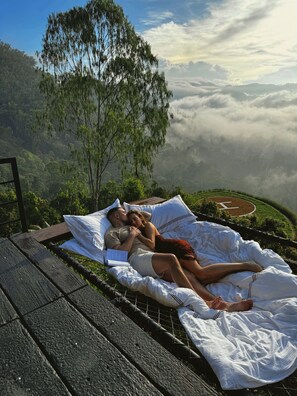 A couple lying on a bed with a view of a mountainous landscape and a tree. - Walaa Kulu – A Villa by 98 Acres (Ella)
