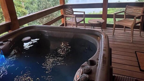 A hot tub on a wooden deck with a view of a lake and forest.