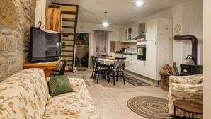 A living room with a sofa, a television, a dining area with chairs, a kitchen with cabinets, and a stone wall. - House Rea is ideal for a retreat in nature, close to the richness of Istria ! (buzet)
