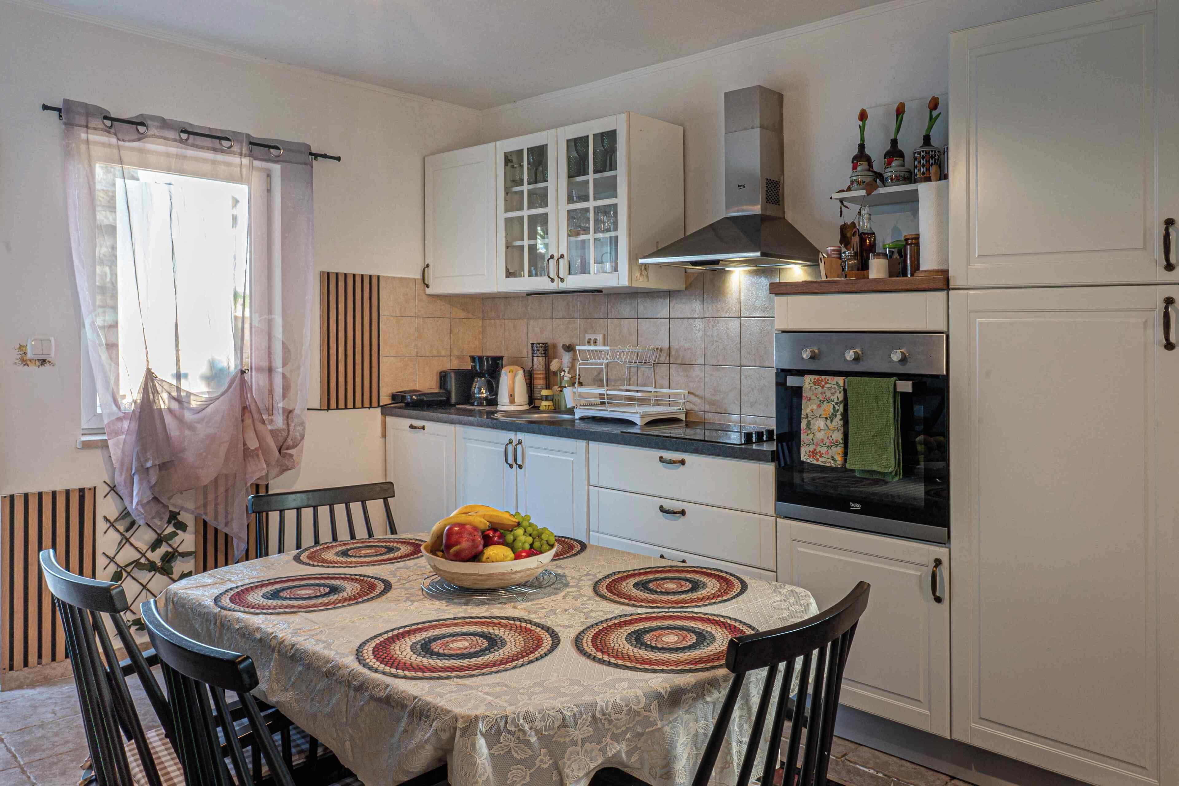 A kitchen with a dining table, chairs, a bowl of fruit, and a stove.