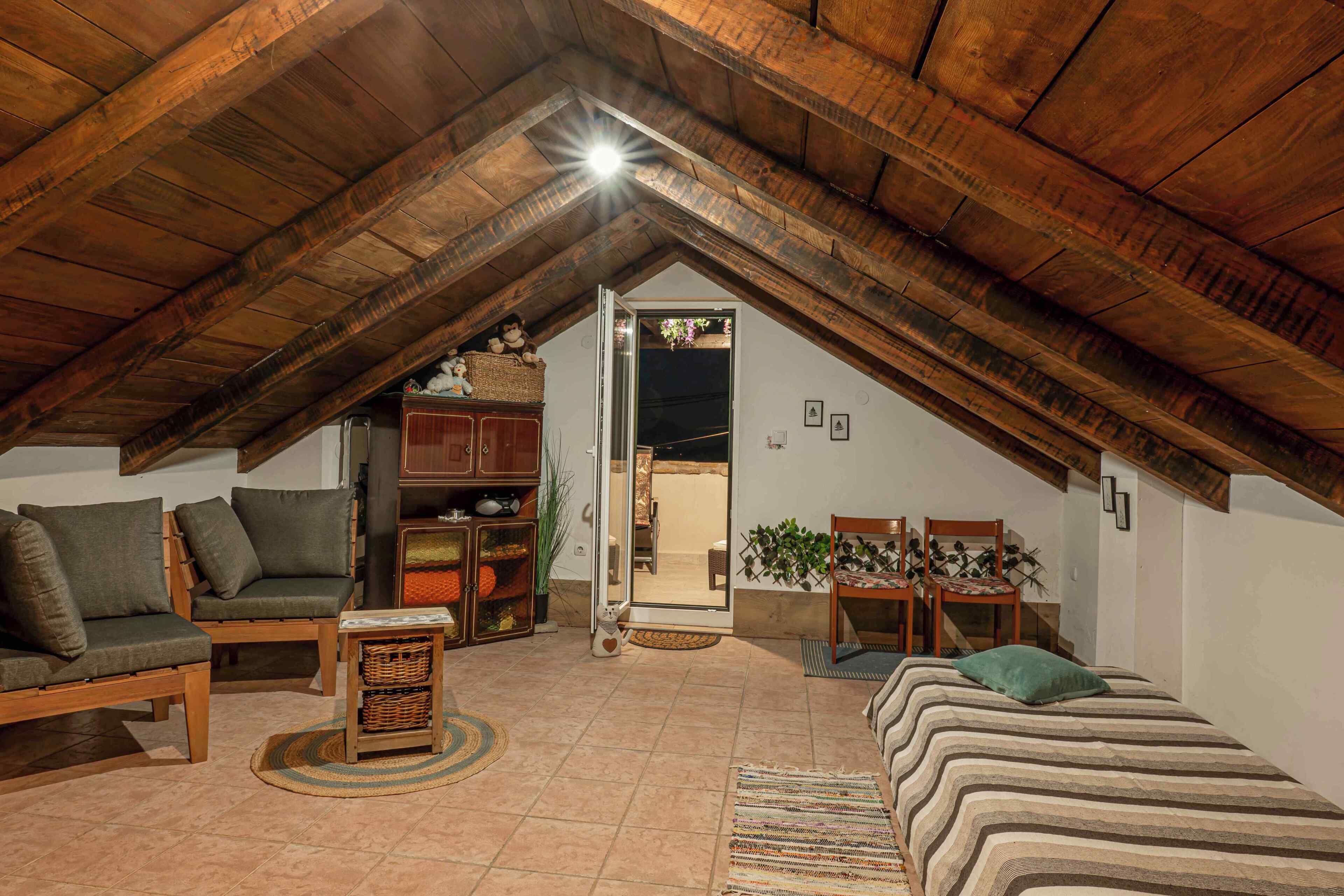 Ein Schlafzimmer im Dachgeschoss mit schrägen Wänden, Holzmöbeln, einem Bett und Blick durch eine geöffnete Tür.
