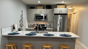 A modern kitchen with a central island, stainless steel appliances, and wooden stools.