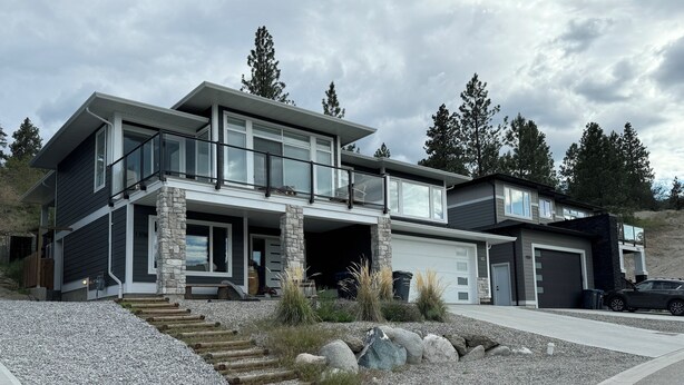 A modern two-story house with a stone facade, large windows, and a garage.