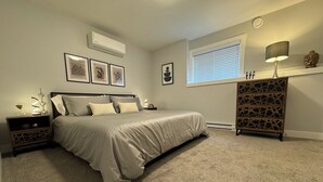 A bedroom with a bed, nightstands, a dresser, wall art, and a window with blinds.