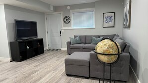 A modern living room with a grey sofa, a black entertainment unit, a globe on a stand, and a large window with blinds.